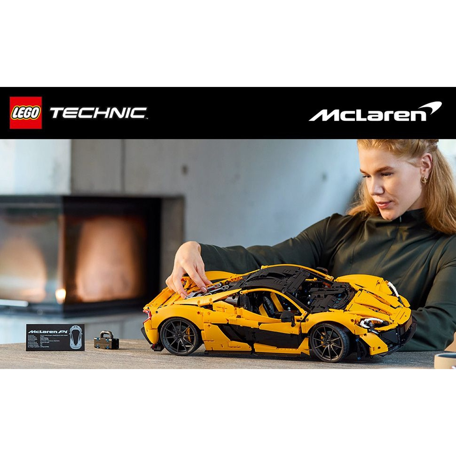 Donna bionda che costruisce un'auto Lego Technic McLaren gialla. Auto nera e gialla su un tavolo, piccola carta e lucchetto visibili.