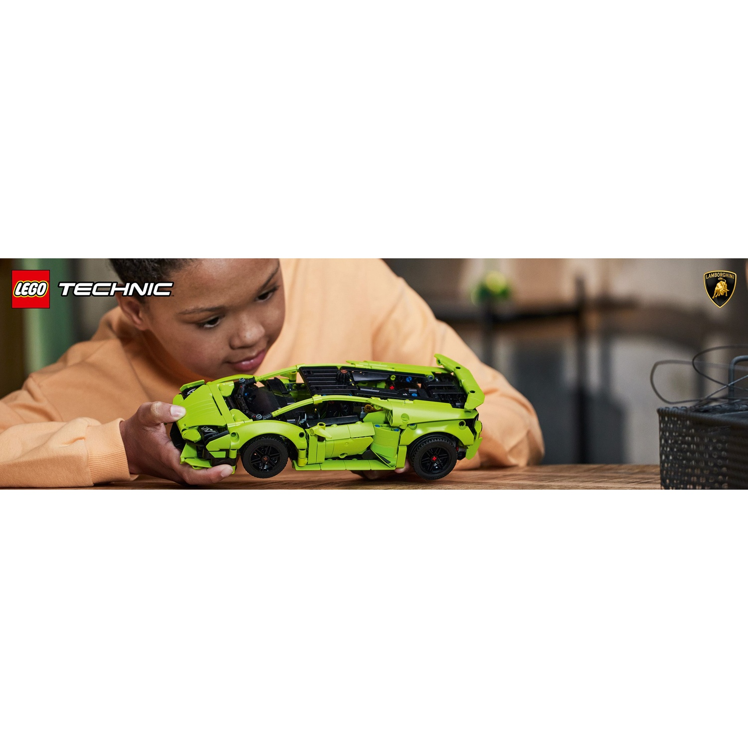 Un bambino tiene in mano una Lamborghini Lego Technic verde lime. L'auto è su un tavolo di legno e il bambino indossa un maglione arancione.