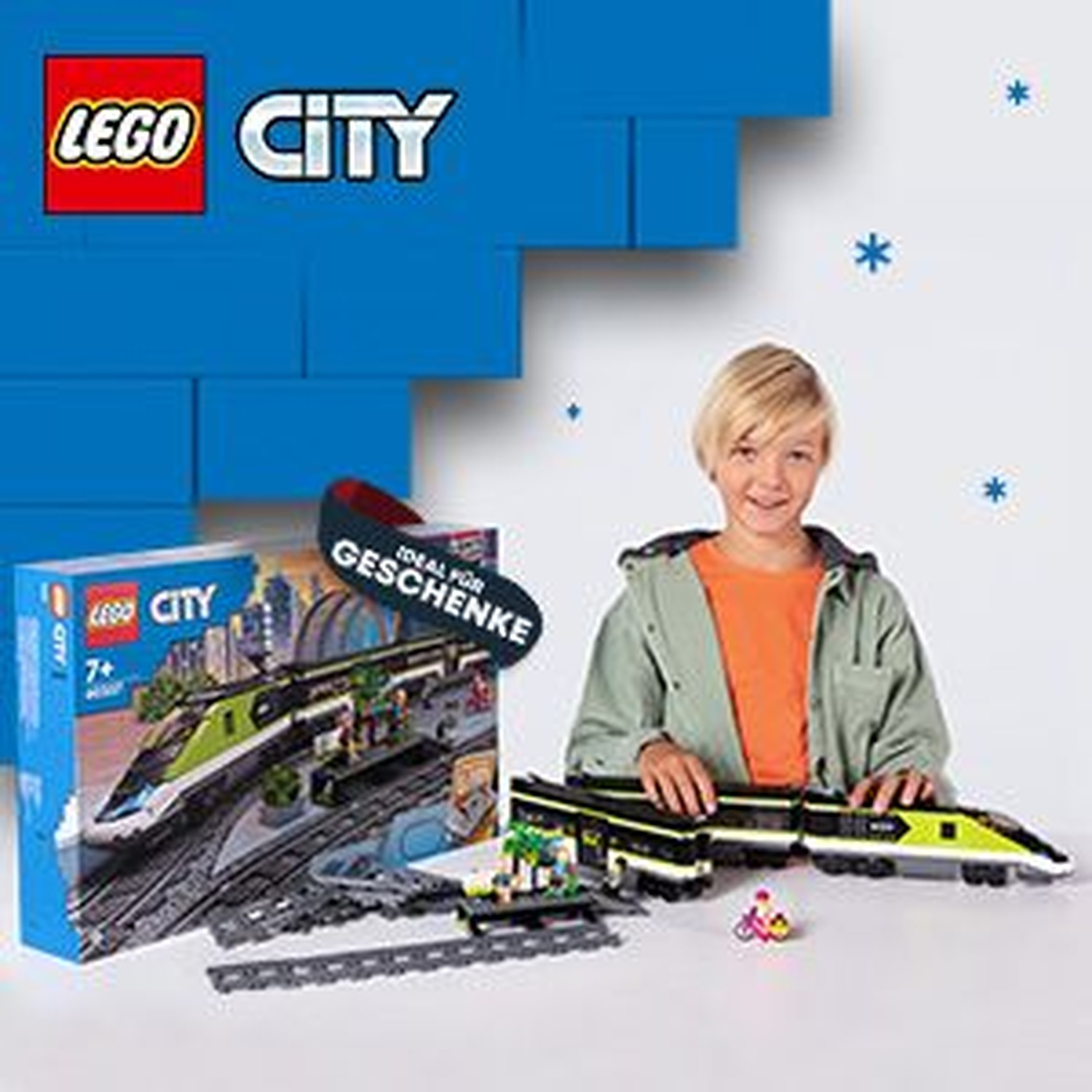 Un bambino con un set di treni Lego City sorride. Una scatola e un treno sono di fronte. Blocchi Lego blu sullo sfondo.