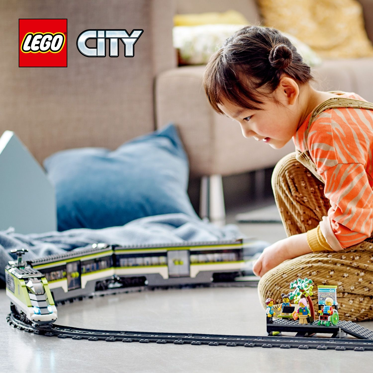 Una bambina gioca con un set di treni Lego. Un treno verde e bianco corre sui binari. Personaggi su una piattaforma.