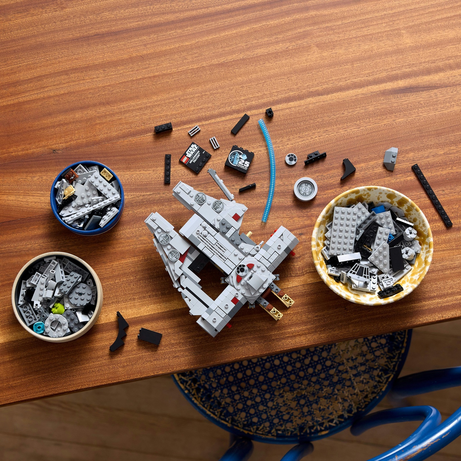 Un set Lego Star Wars Millennium Falcon parzialmente assemblato su un tavolo di legno, con pezzi sparsi e ciotole di mattoncini Lego.
