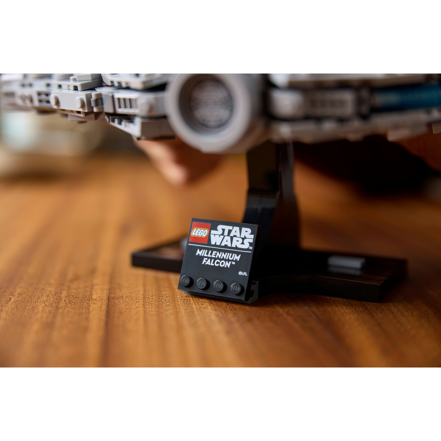 Un modello Lego Star Wars Millennium Falcon su una superficie di legno. Un supporto nero tiene il modello e una targa Lego.