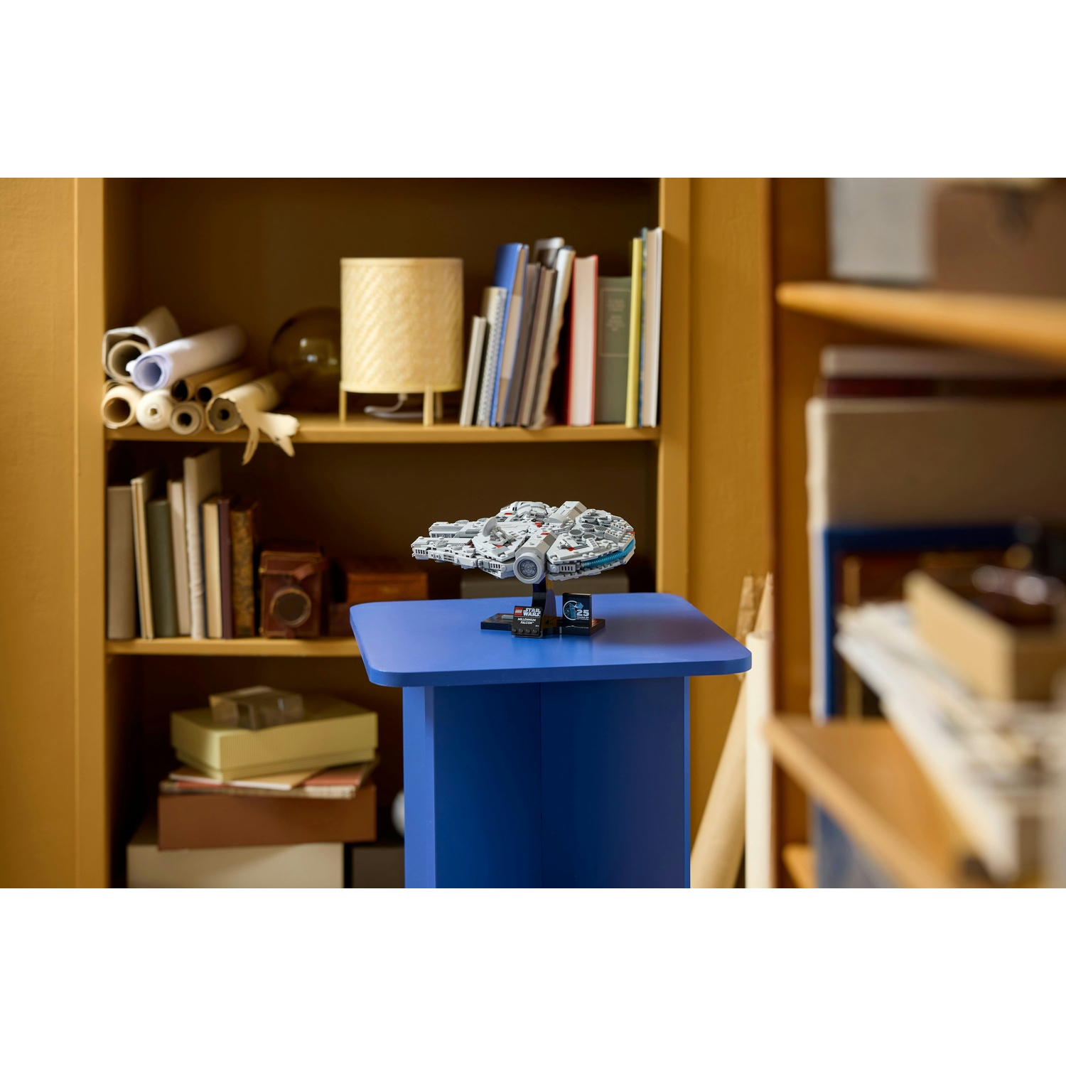 Un modello Lego di Millennium Falcon di Star Wars è su un tavolo blu. Librerie piene di libri e decorazioni sullo sfondo.
