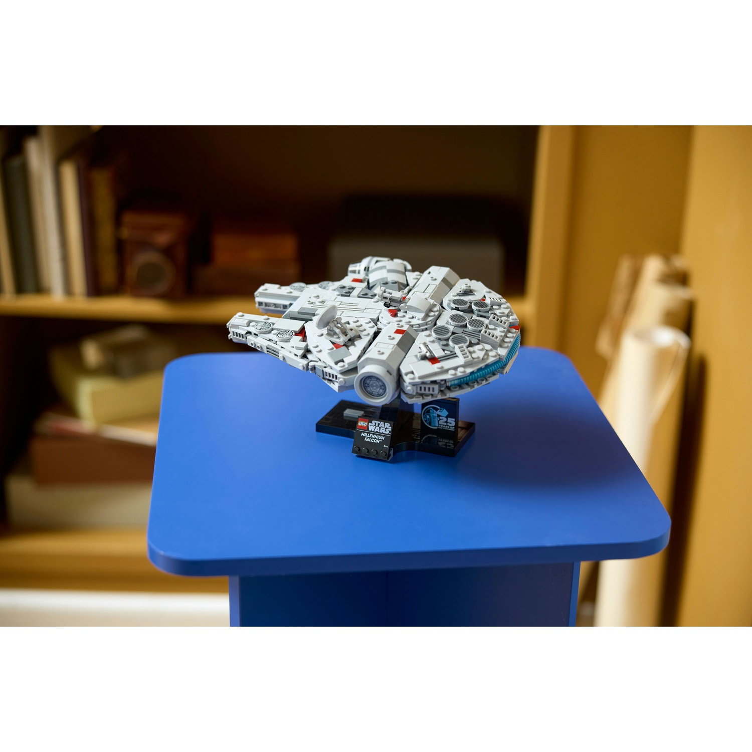 Un modello Lego del Millennium Falcon è su un tavolo blu. Dietro c'è una libreria. Il modello è grigio e bianco.
