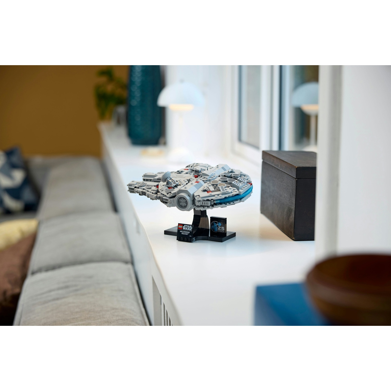 Un set Lego Millennium Falcon di Star Wars su una superficie bianca. Sullo sfondo un divano, un vaso turchese e una lampada.