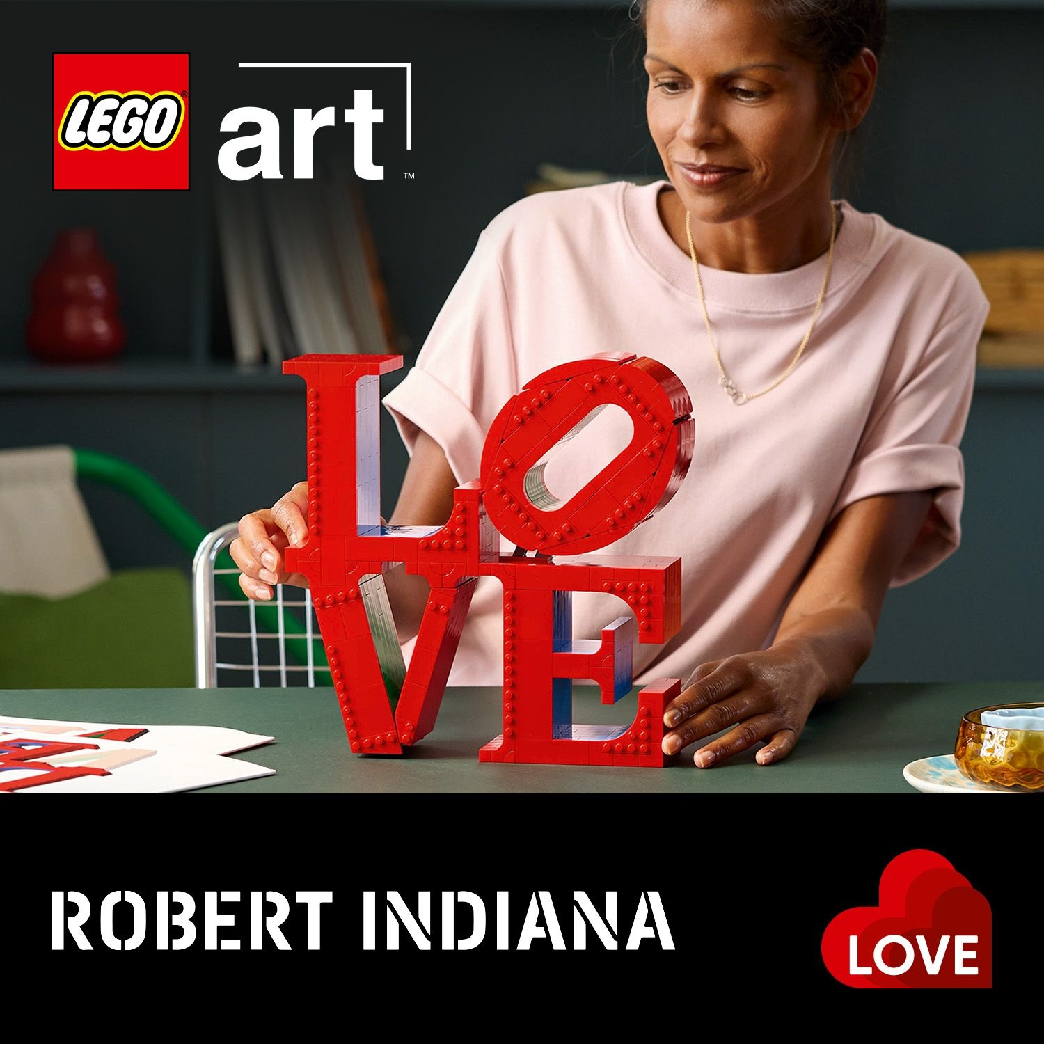 Donna che tiene la scultura rossa LEGO art 'LOVE'. Il logo 'LEGO art' è in alto a sinistra. L'artista è Robert Indiana.