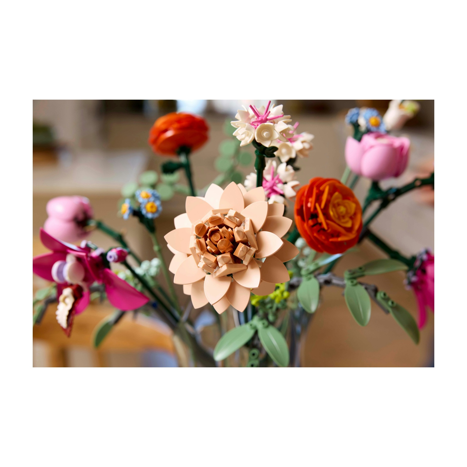 Un bouquet di fiori Lego colorati in un vaso di vetro. Include fiori arancioni, rosa, crema e blu. Sono visibili foglie e steli verdi.
