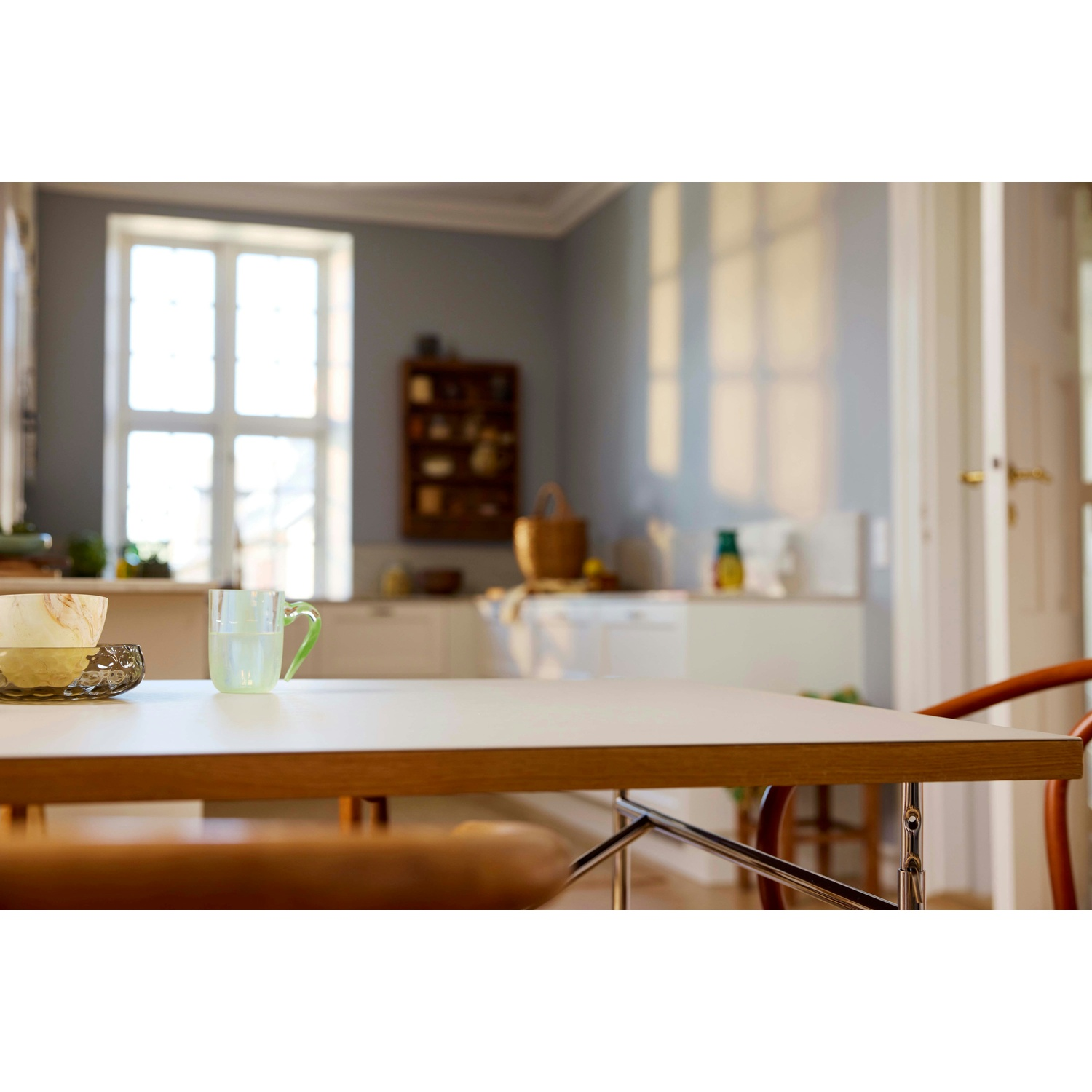 Un tavolo con una tazza di vetro e delle ciotole in una cucina. Sullo sfondo c'è una finestra, un armadio e una sedia sono visibili.