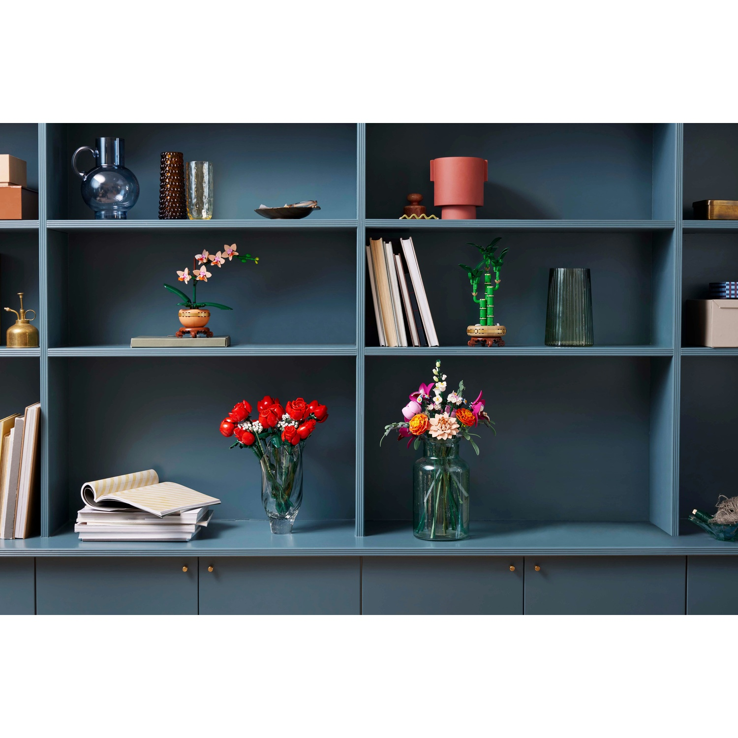 Una mensola blu mostra vasi, fiori, libri e oggetti decorativi. Rose rosse, orchidee e bambù sono tra le composizioni floreali.