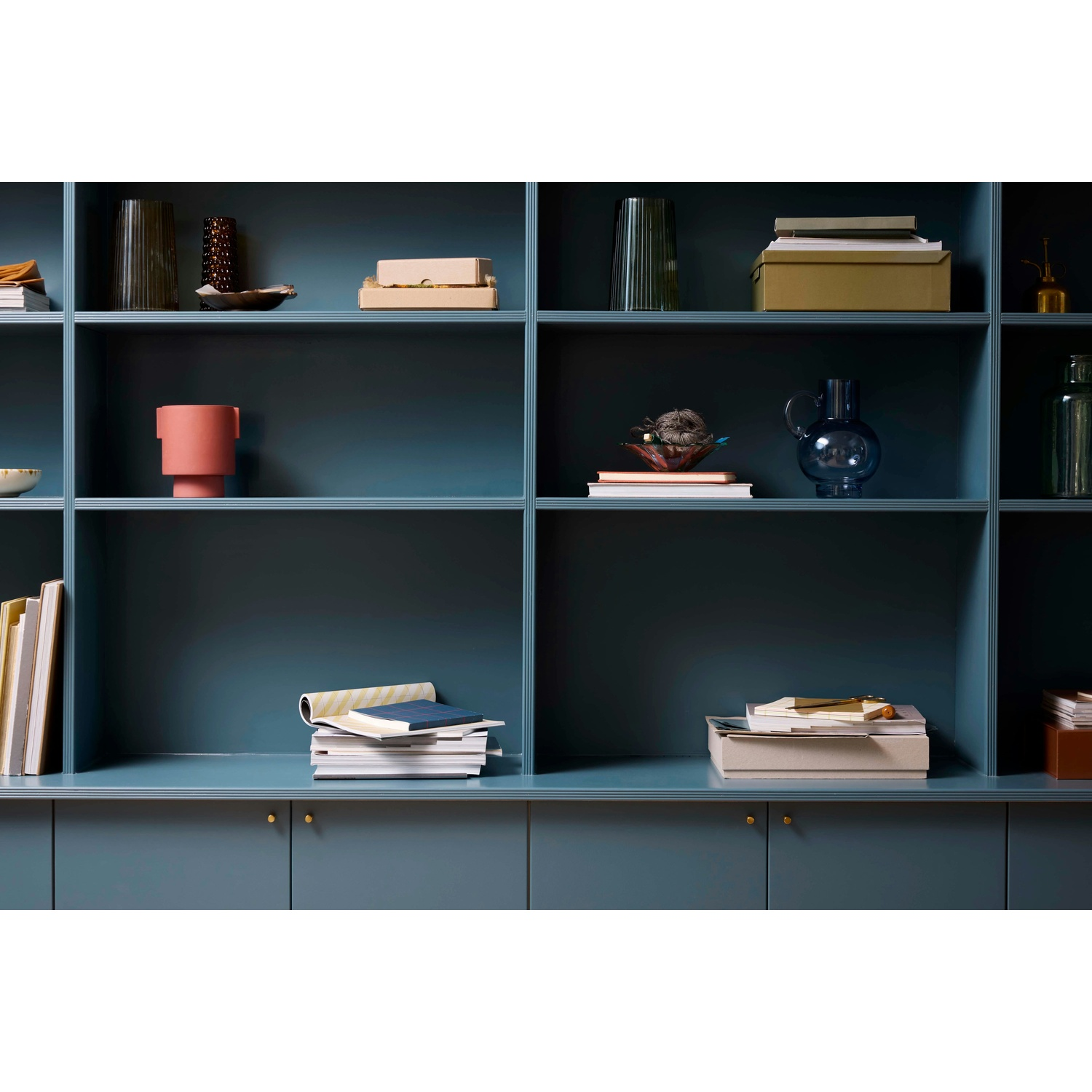 Una libreria color teal con vari oggetti. Vasi, libri, scatole e oggetti decorativi sono disposti sugli scaffali.