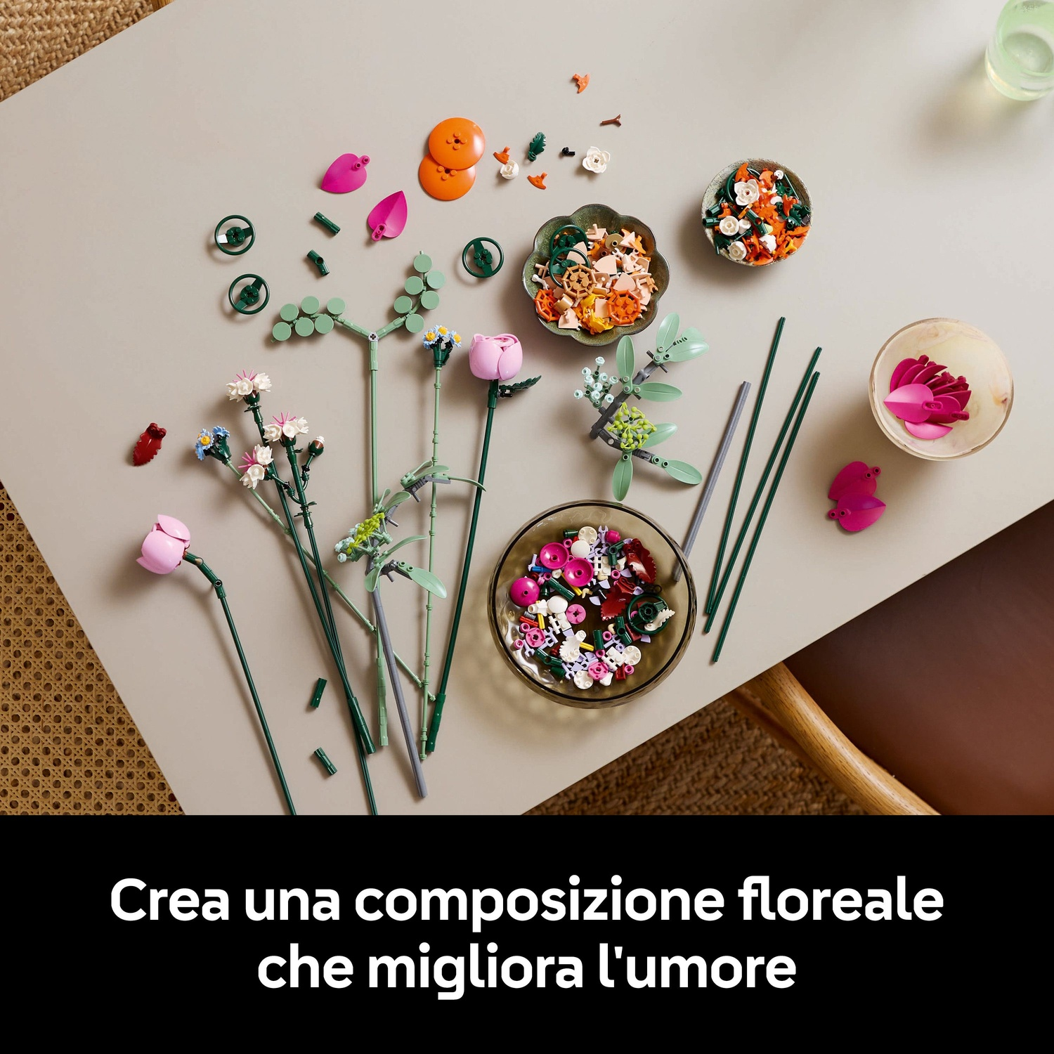 Vista dall'alto dei componenti di un'arrangiamento floreale su un tavolo. Include parti di fiori in plastica rosa, bianca, arancione e verde e ciotole.