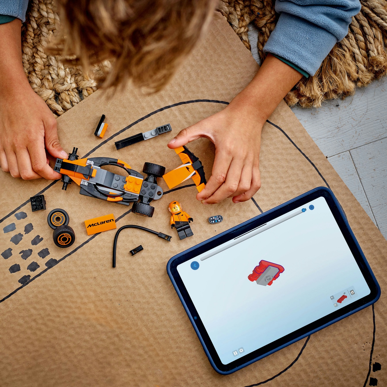 Un bambino assembla una macchina da corsa Lego, seguendo le istruzioni su un tablet. L'auto è arancione e nera, con pezzi di ricambio sparsi.