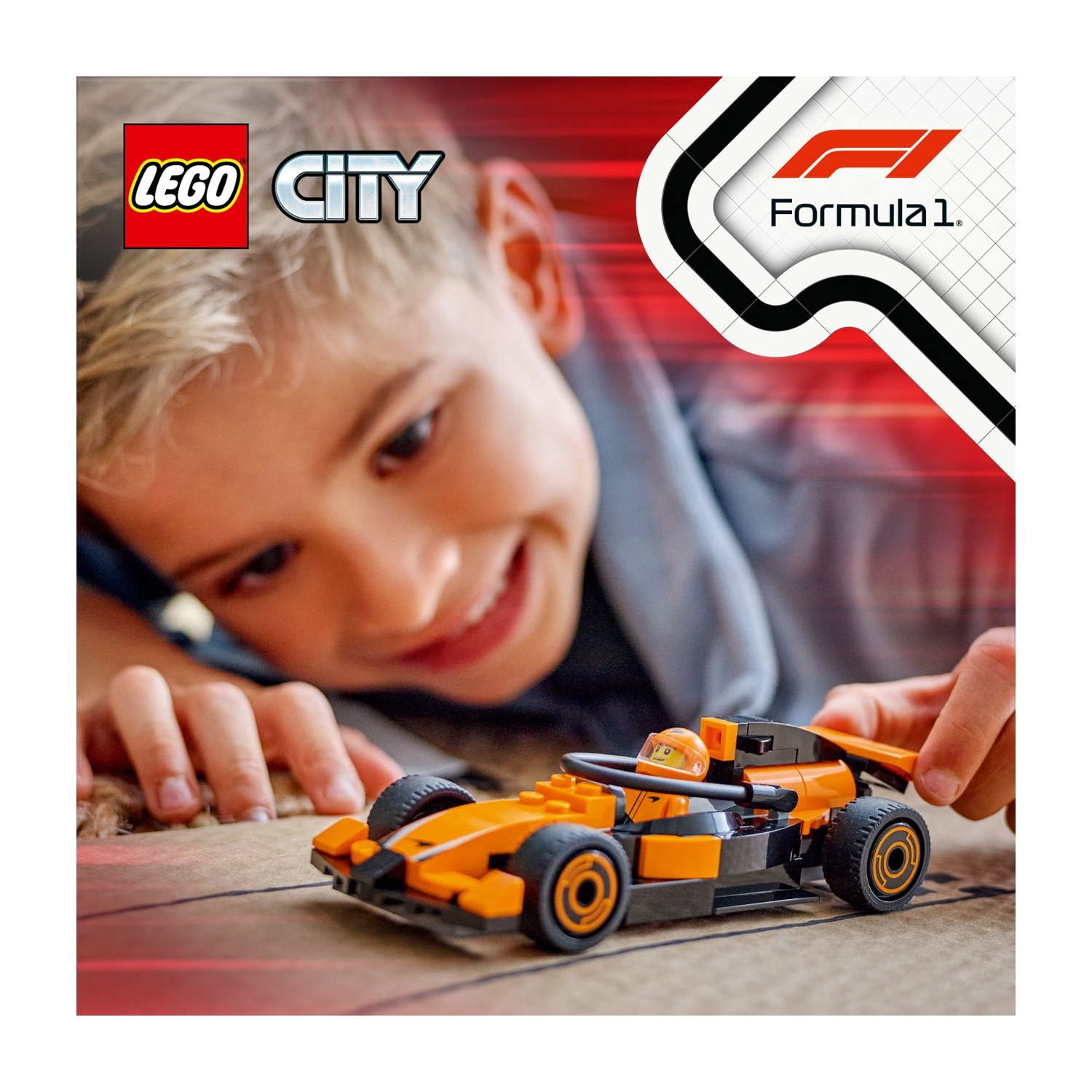Un ragazzo sorride, guardando un'auto da corsa Lego arancione e nera. L'auto è su una superficie marrone. Il logo Lego City è visibile.