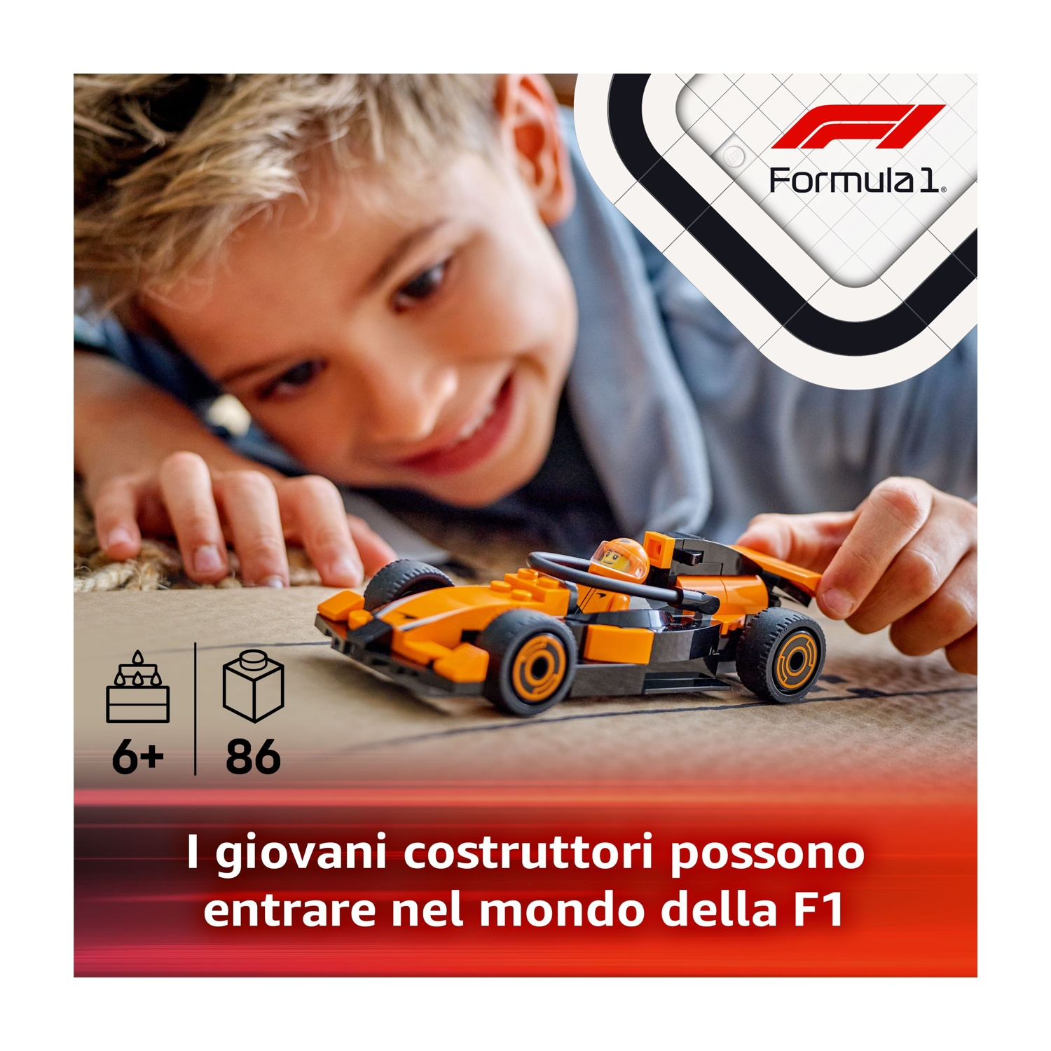 Un ragazzo sorride a un'auto da corsa giocattolo arancione e nera. L'auto è su una scatola. Logo Formula 1 sullo sfondo.