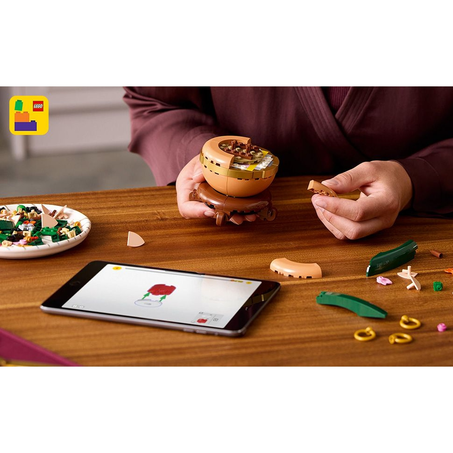 Una persona che assembla cibo Lego. Un tablet mostra le istruzioni. C'è un piatto di ingredienti Lego e pezzi sparsi sul tavolo di legno.