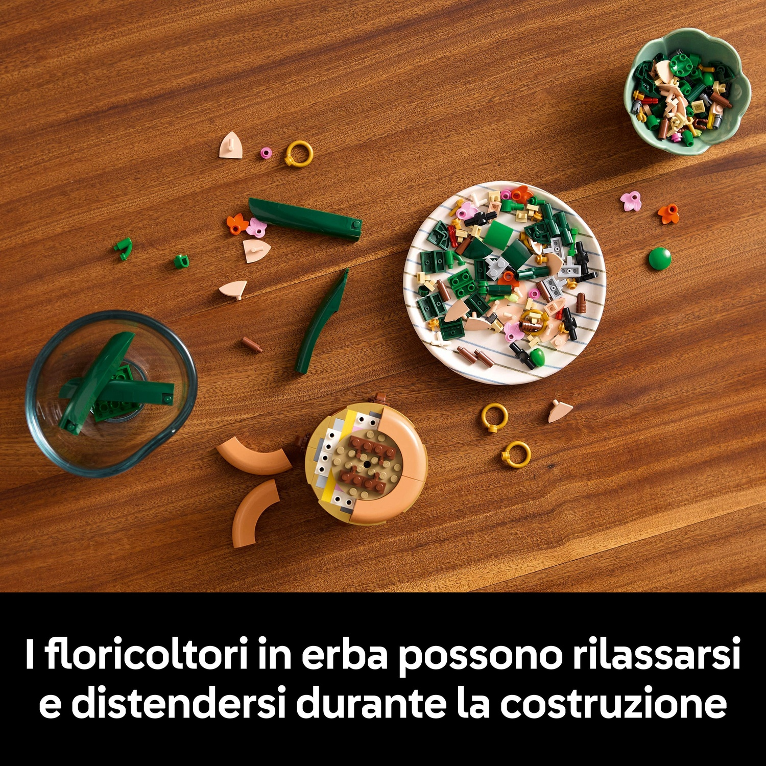 Tavolo di legno con pezzi Lego sparsi, tra cui elementi verdi, beige, rosa e marroni, in una ciotola e su un piatto.