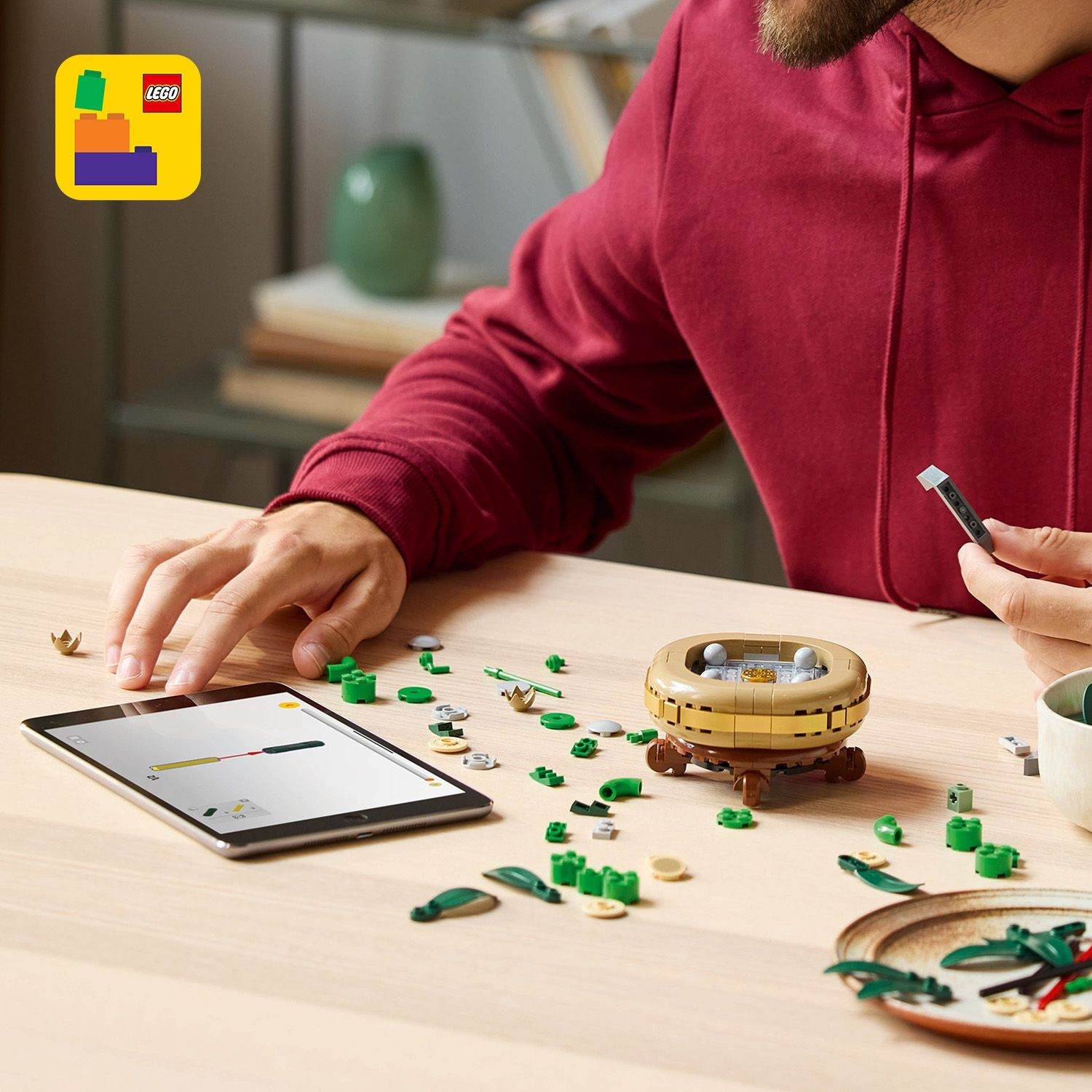 Persona assembla Lego. Tablet mostra istruzioni. Pezzi Lego e struttura finita sul tavolo.