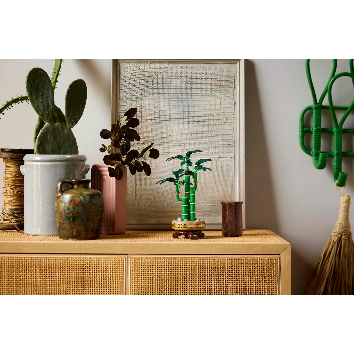 Un mobile in legno con piante e decorazioni. Cactus, vasi, una pianta di bambù e una scopa sono visibili.