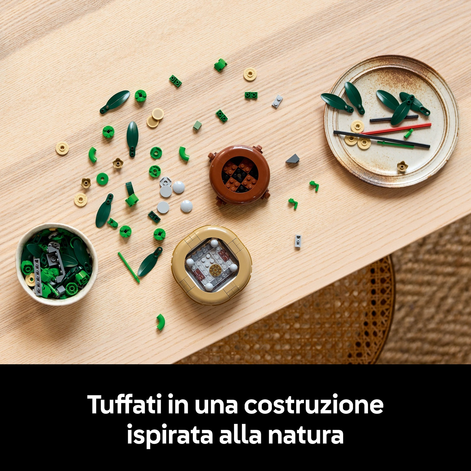Tavolo in legno con pezzi Lego sparsi: foglie verdi, strutture Lego circolari e quadrate e una ciotola piena di pezzi.