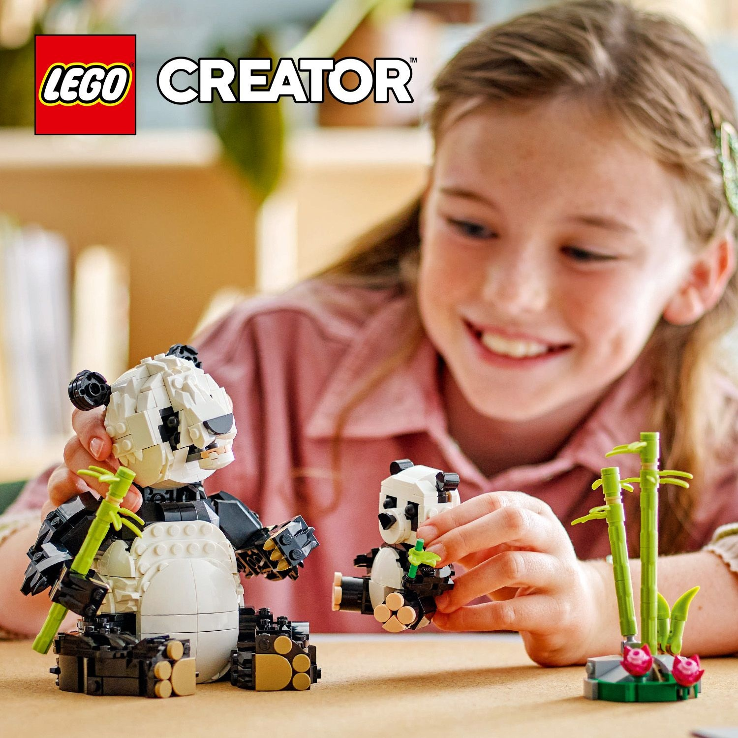 Una ragazza sorride, gioca con i modelli di panda LEGO. Due panda e bambù su un tavolo di legno. Il logo LEGO Creator in alto a sinistra.