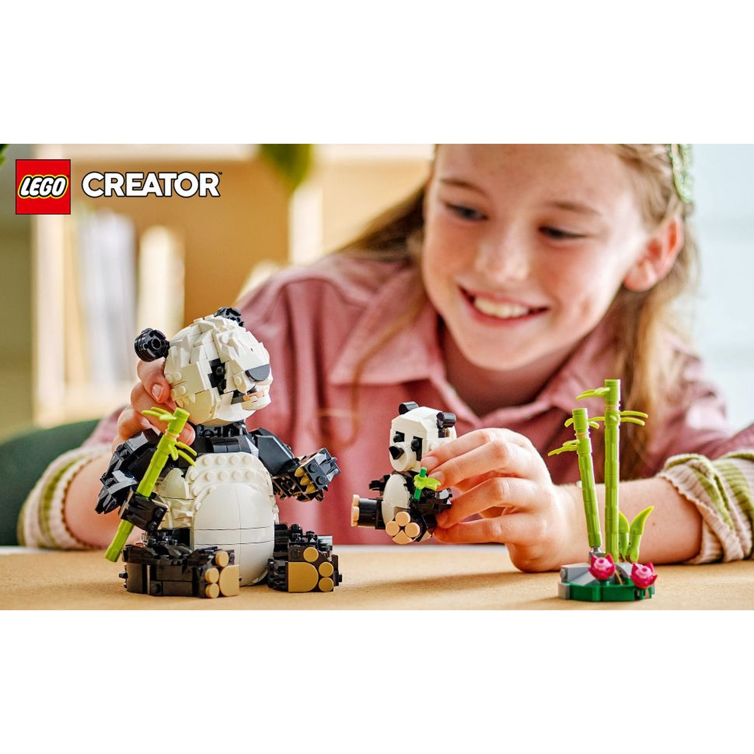 Una ragazza sorride, tenendo panda Lego con bambù. Due panda sono su un tavolo. Un panda adulto e un cucciolo. Il logo LEGO CREATOR è visibile.
