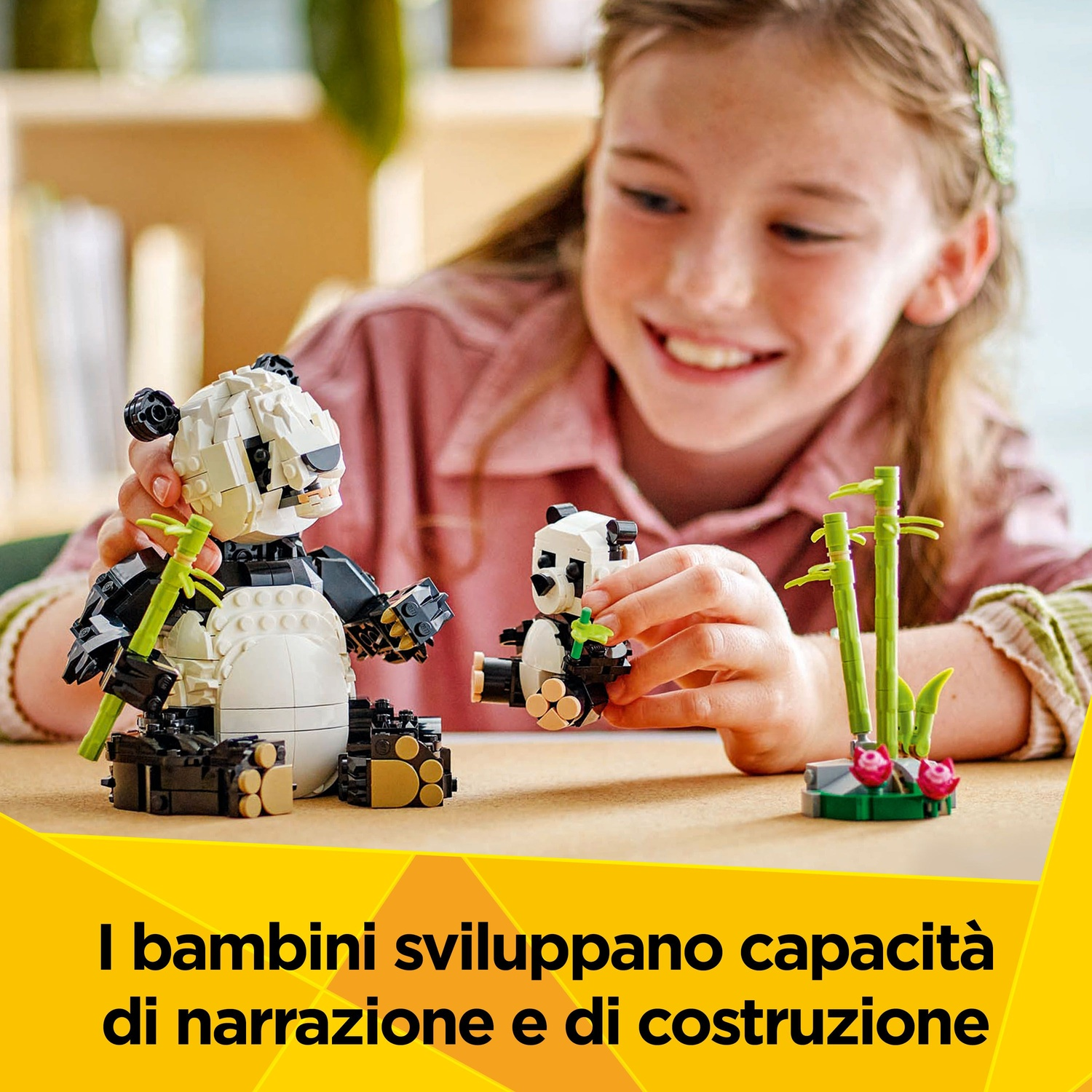 Una ragazza gioca con set Lego di panda, uno grande e uno piccolo. Sul tavolo ci sono anche bambù e fiori. La ragazza sorride.