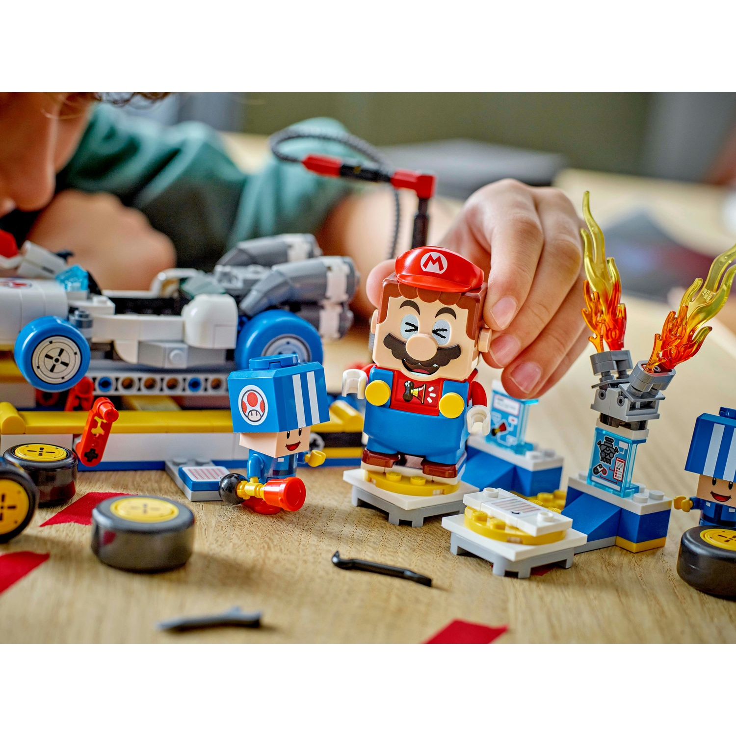 Un bambino gioca con un set Lego di Mario. Mario e altri personaggi sono su una superficie di legno con un'auto, fiamme e pneumatici.