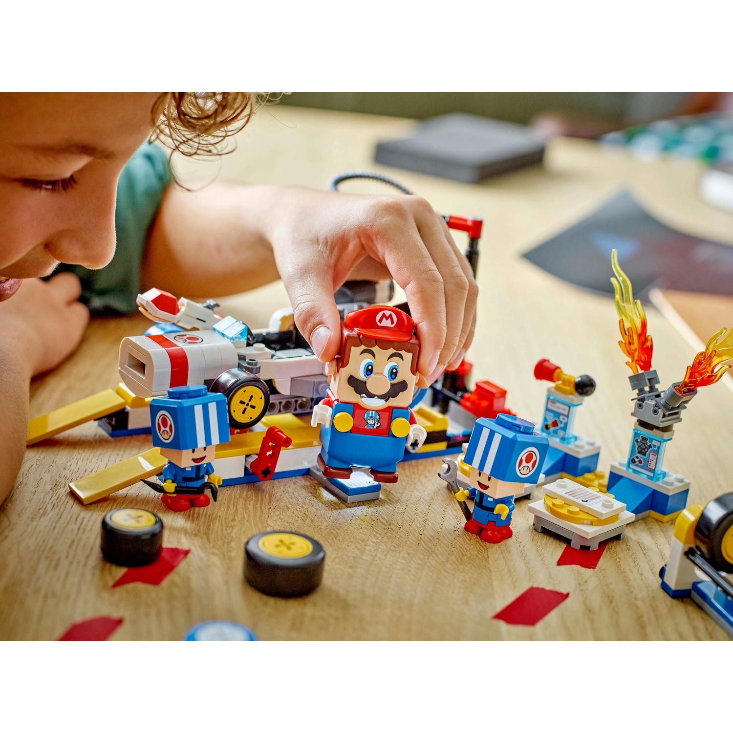Un bambino gioca con un set Lego di Mario. Mario e altri due personaggi sono vicino a un piccolo veicolo. Altri pezzi Lego sono visibili.