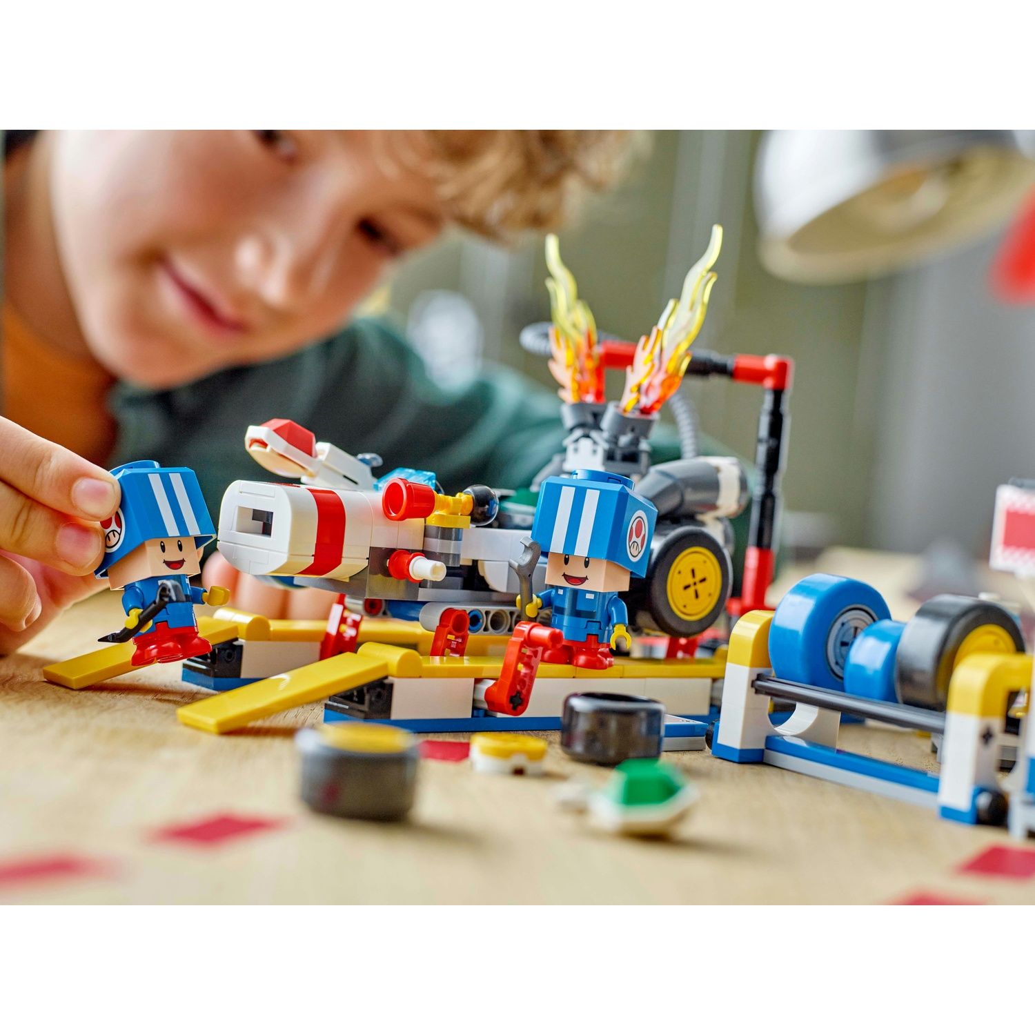 Un bambino gioca con un set Lego. Il set include personaggi giocattolo, un veicolo con fiamme e altri componenti colorati.