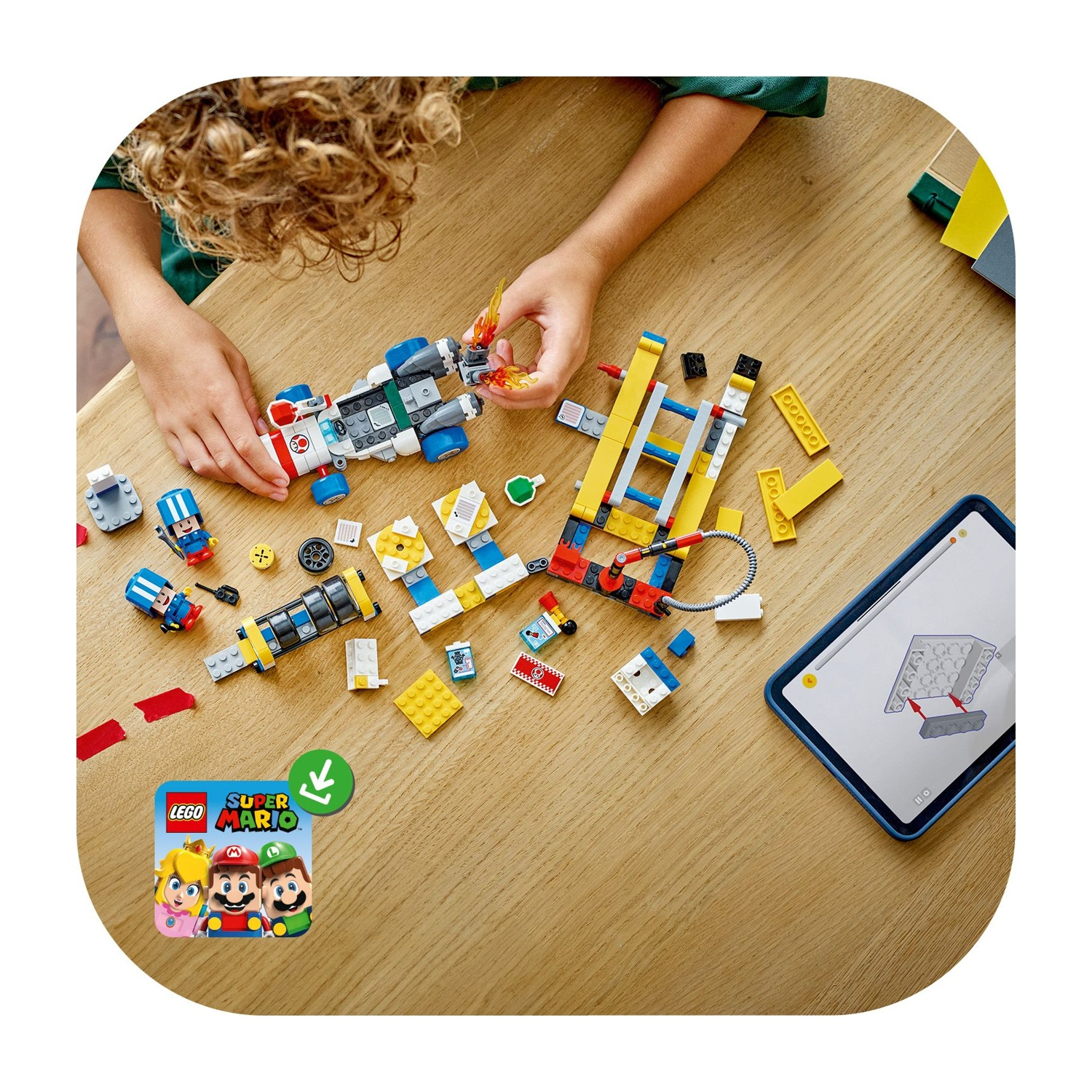Un bambino sta costruendo un set Lego, a tema Super Mario, su un tavolo di legno. Sono visibili vari pezzi Lego e un tablet con le istruzioni.