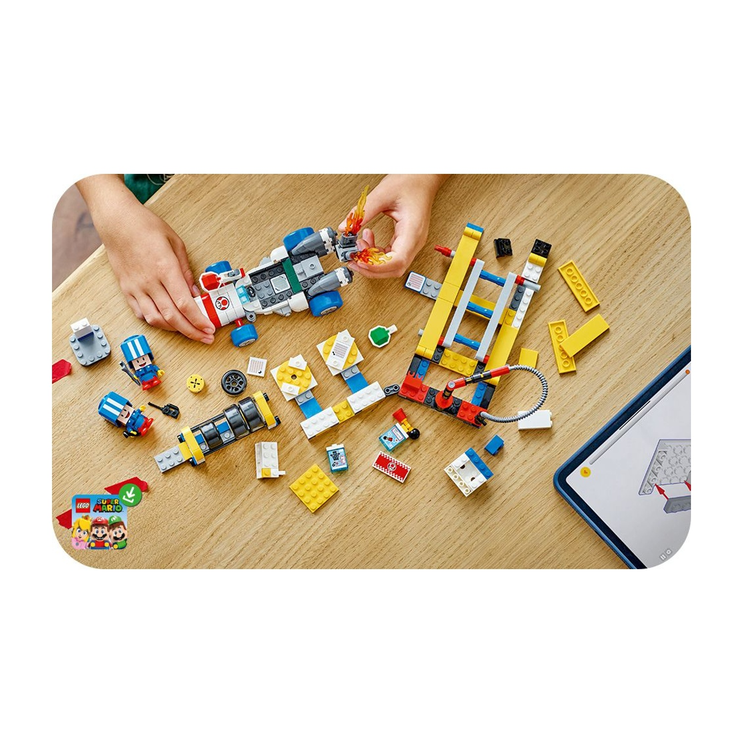 Mani che assemblano il set LEGO Super Mario su un tavolo di legno. I componenti includono un'astronave, personaggi e istruzioni su un tablet.