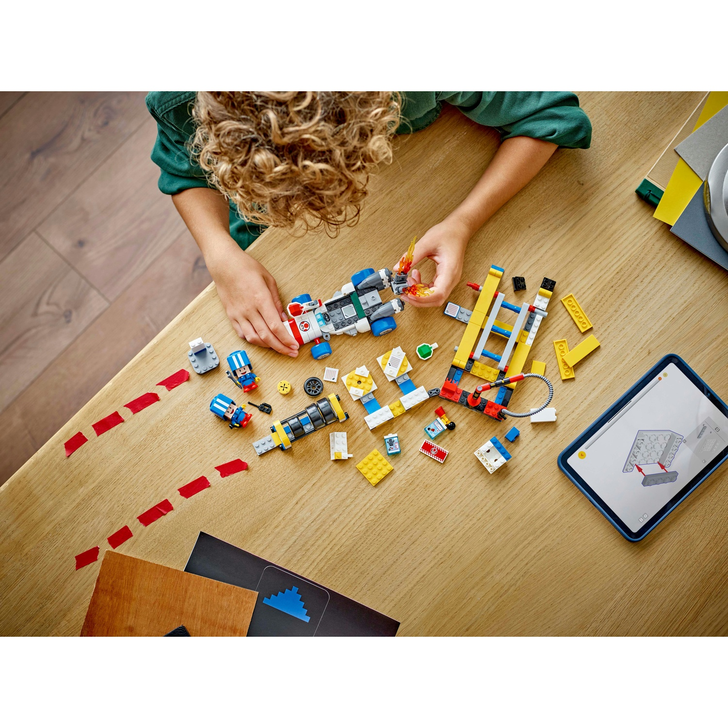 Un bambino assembla un set Lego su un tavolo di legno. Il set include un'auto da corsa, una pista e un tablet con le istruzioni.
