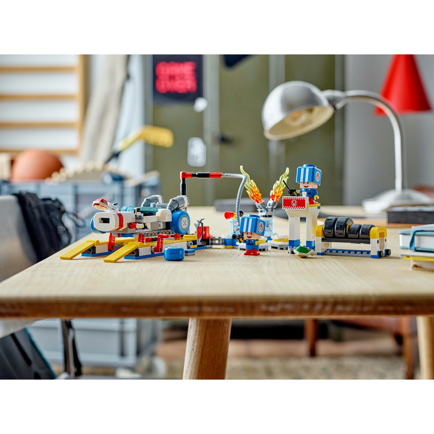 Un set Lego è su un tavolo di legno. Presenta un'auto, personaggi e un elemento fuoco. Lo sfondo mostra una lampada e decorazioni murali.