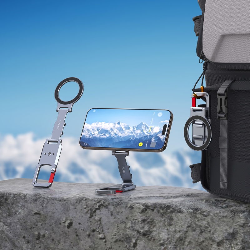 Bir stand üzerinde bir telefon, bir sırt çantasına takılı telefon tutucu, arka planda bir dağ silsilesi. Gökyüzü mavi.