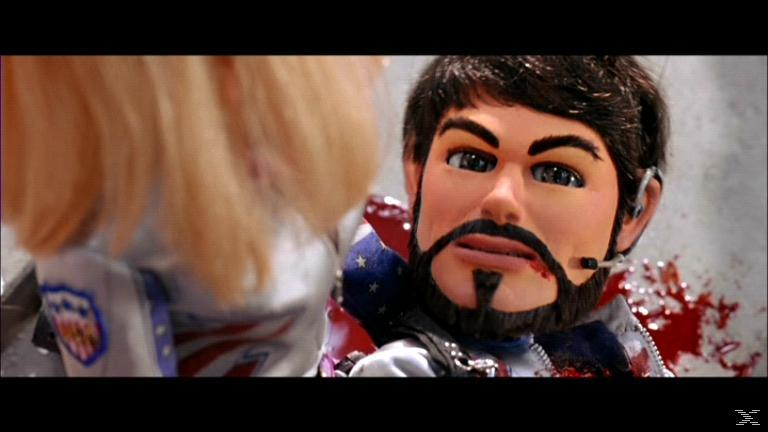 Eine Marionette mit Bart und Blut im Gesicht. Eine andere Marionette ist teilweise sichtbar. Blut spritzt an die Wand.