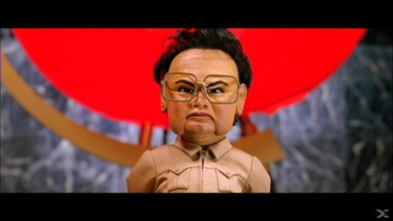 Eine Marionette eines Mannes mit Brille und Stirnrunzeln. Im Hintergrund eine rote Flagge, mit einer goldenen Form.