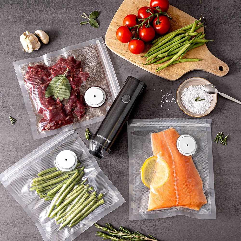 Draufsicht auf Lebensmittel. Enthält Fleisch, Fisch, grüne Bohnen, Tomaten und Knoblauch, alles vakuumverpackt, und ein Vakuumiergerät.