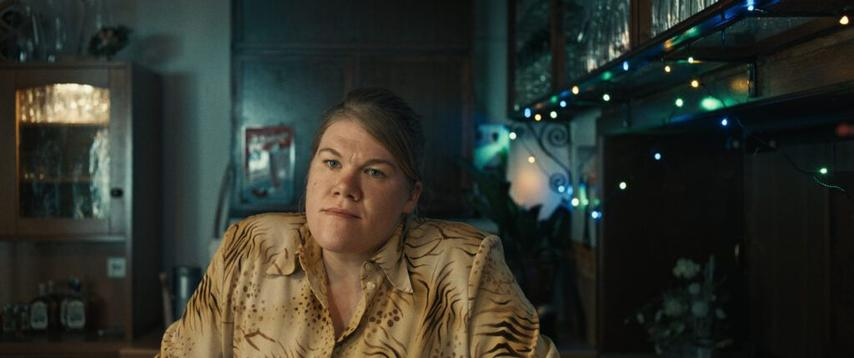 Eine Frau in einem gemusterten Hemd schaut in die Kamera. Lichter und Schränke sind im Hintergrund.