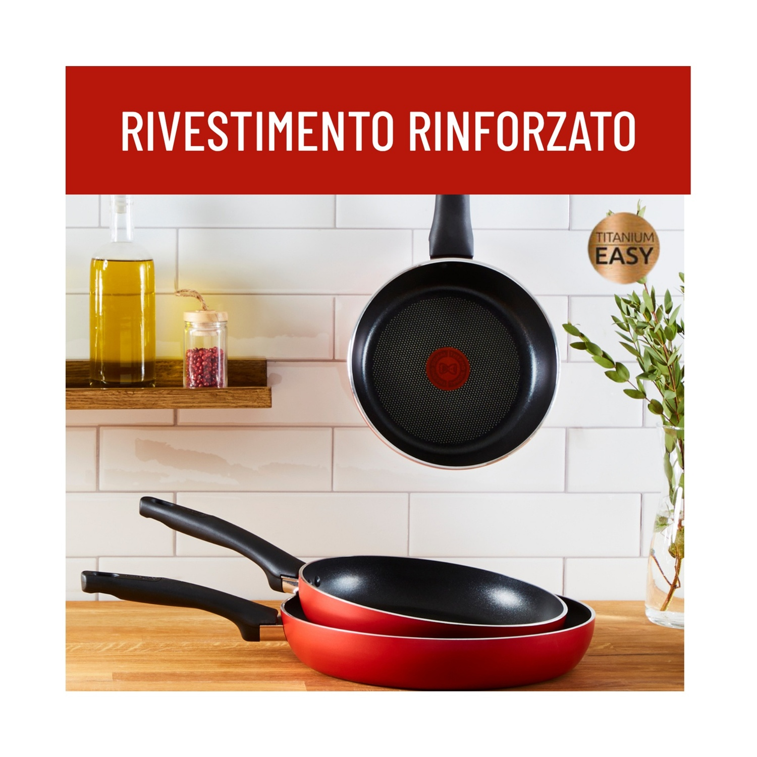 Due padelle, una rossa, una nera, impilate. Una bottiglia di olio d'oliva e spezie su uno scaffale. Una padella appesa.