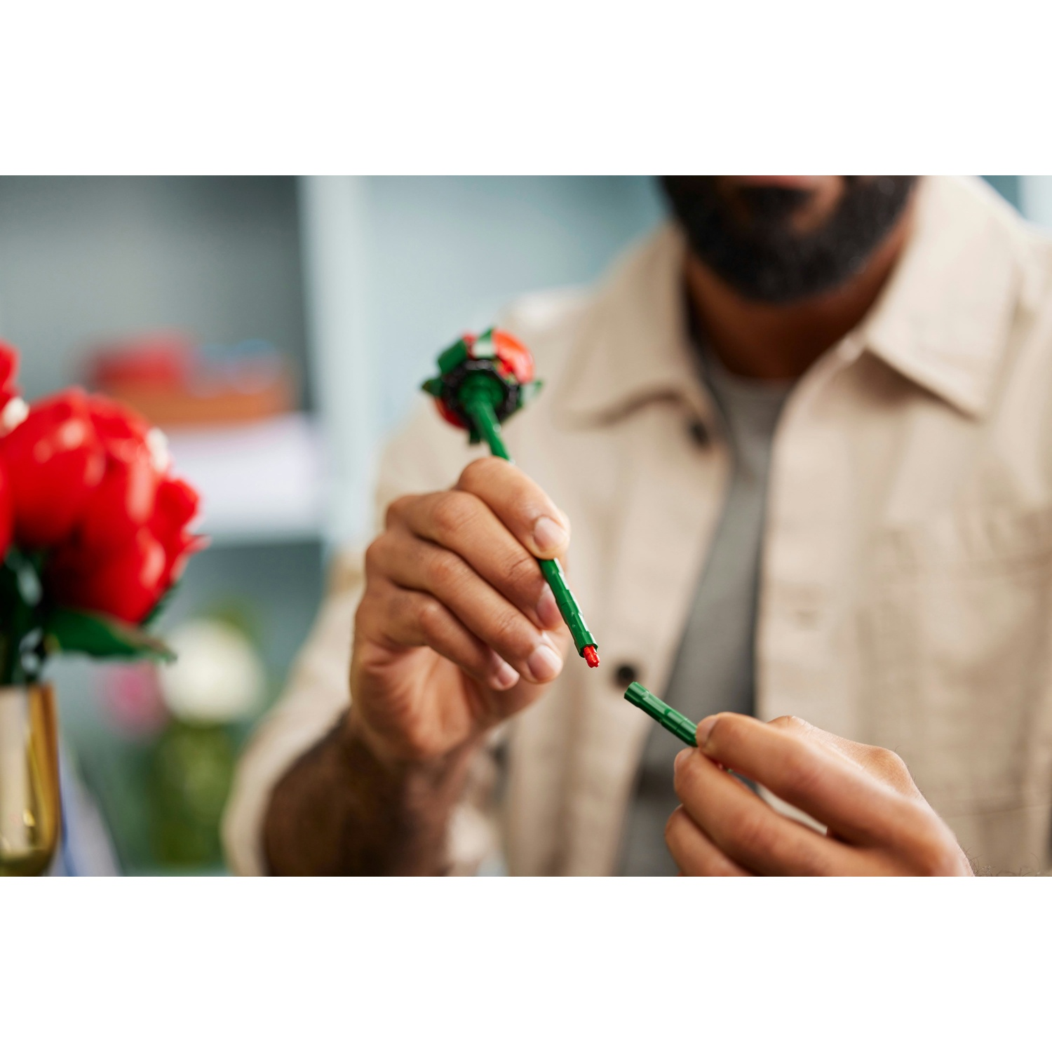 Una persona che assembla una rosa Lego. Tiene uno stelo verde con un bocciolo rosso. Un altro pezzo di stelo nell'altra mano.