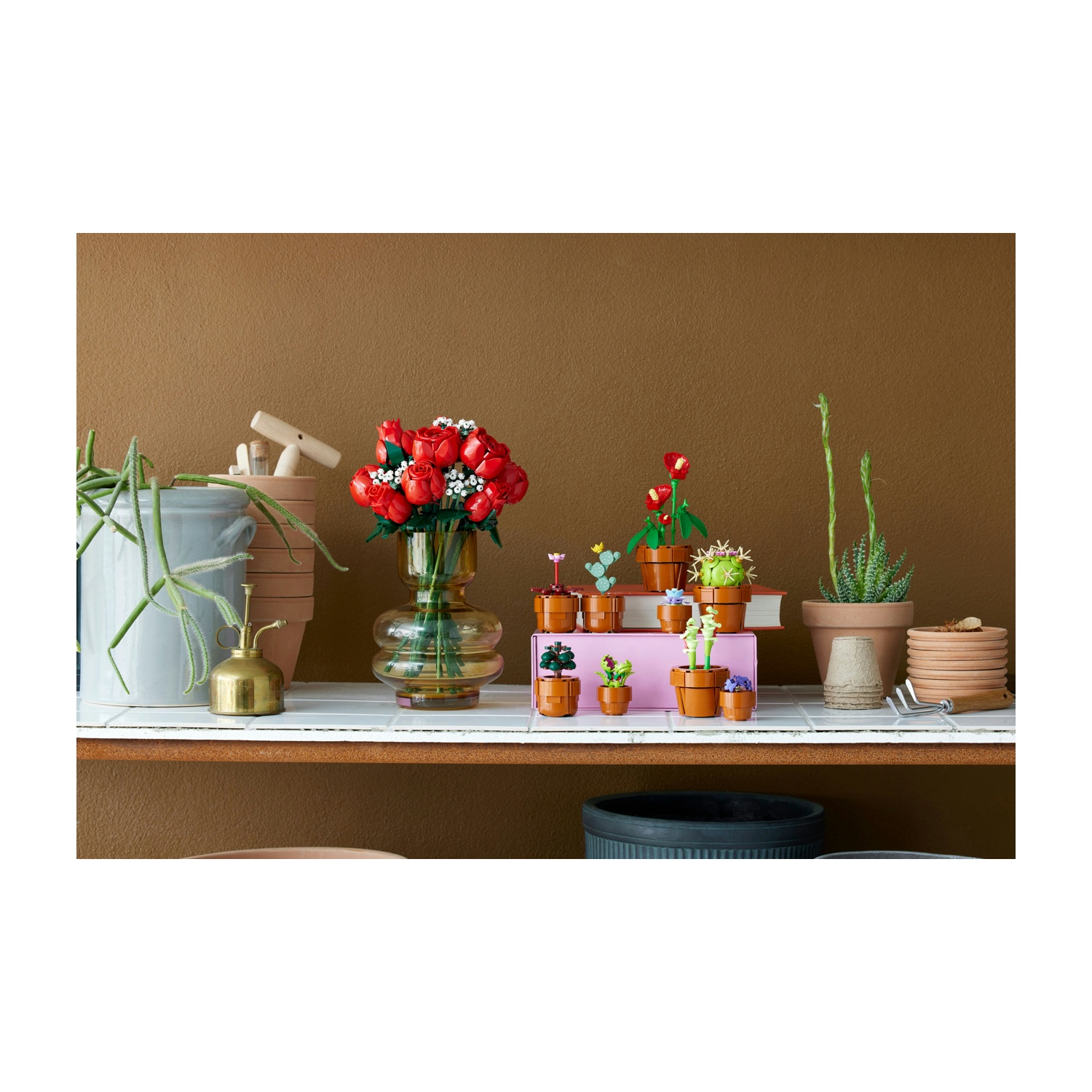 Scaffale con fiori e piante Lego in vaso. Un vaso di rose rosse accanto ad altre piante Lego. Muro marrone sullo sfondo.