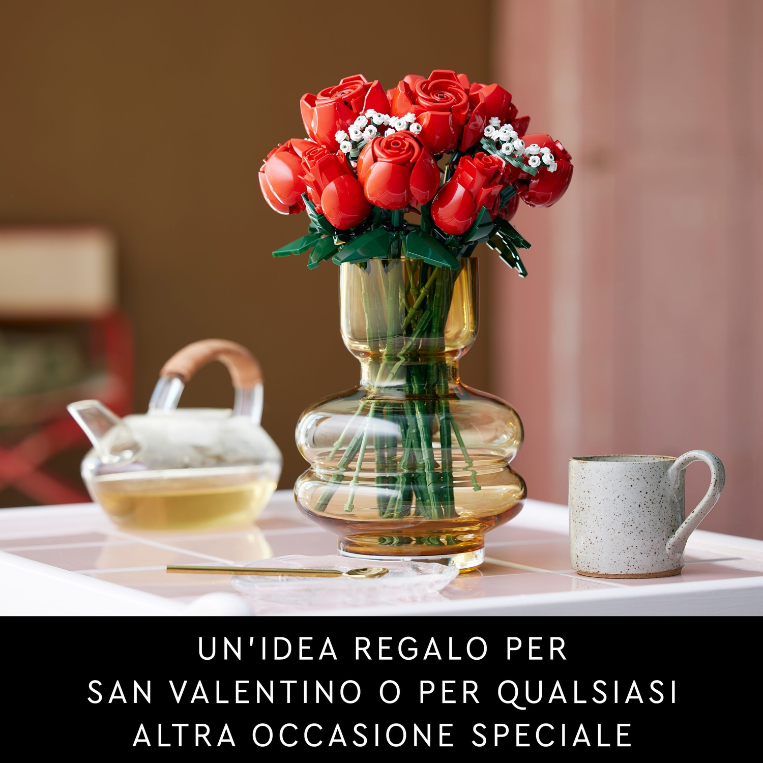 Un vaso con fiori di rose Lego rosse. Una teiera e una tazza sono sul vassoio. Il testo dice: 'Un'idea regalo per San Valentino o per qualsiasi altra occasione speciale'.