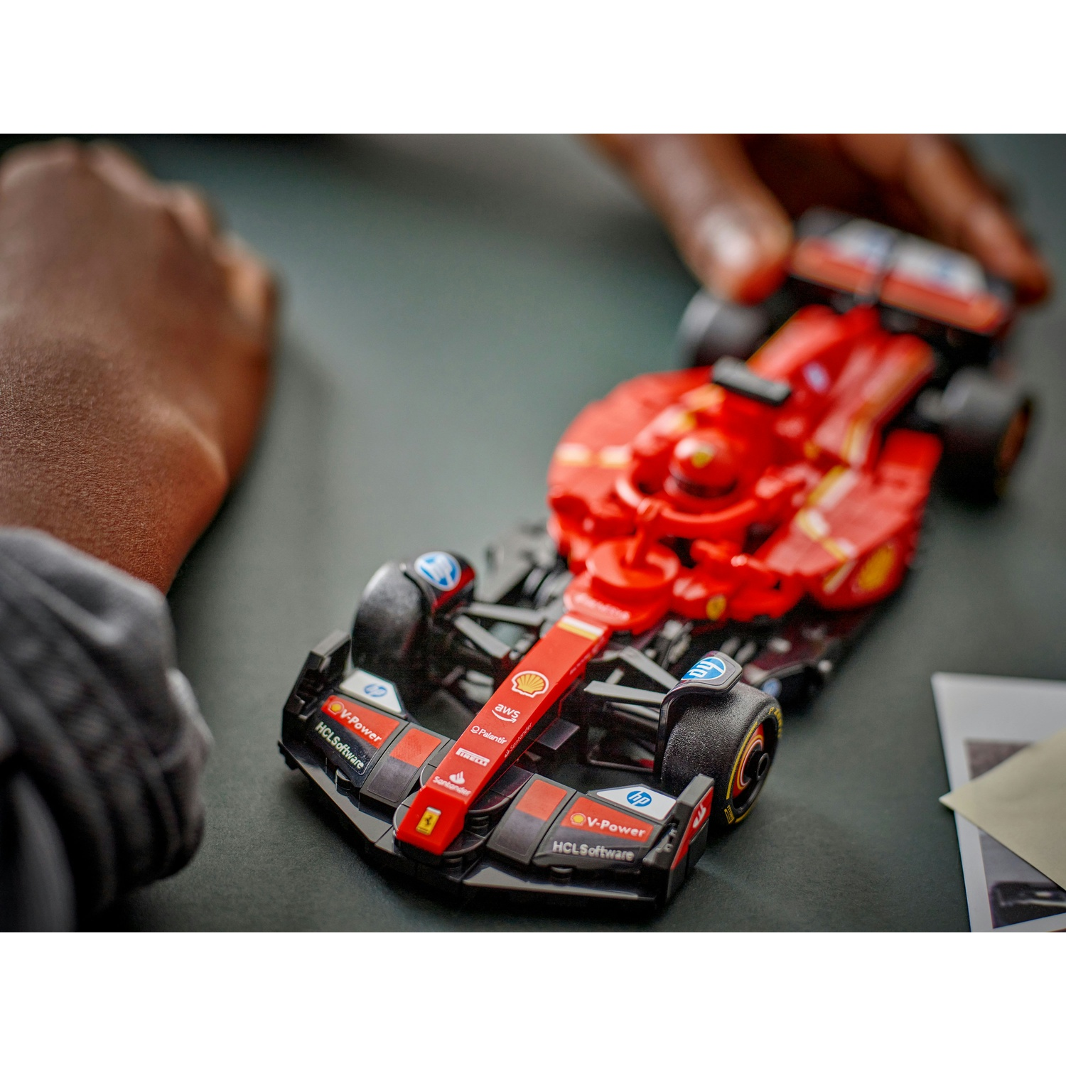Un'auto giocattolo rossa di Formula 1 è tenuta in mano. L'auto ha loghi di sponsor e pneumatici neri. Poggia su una superficie scura.