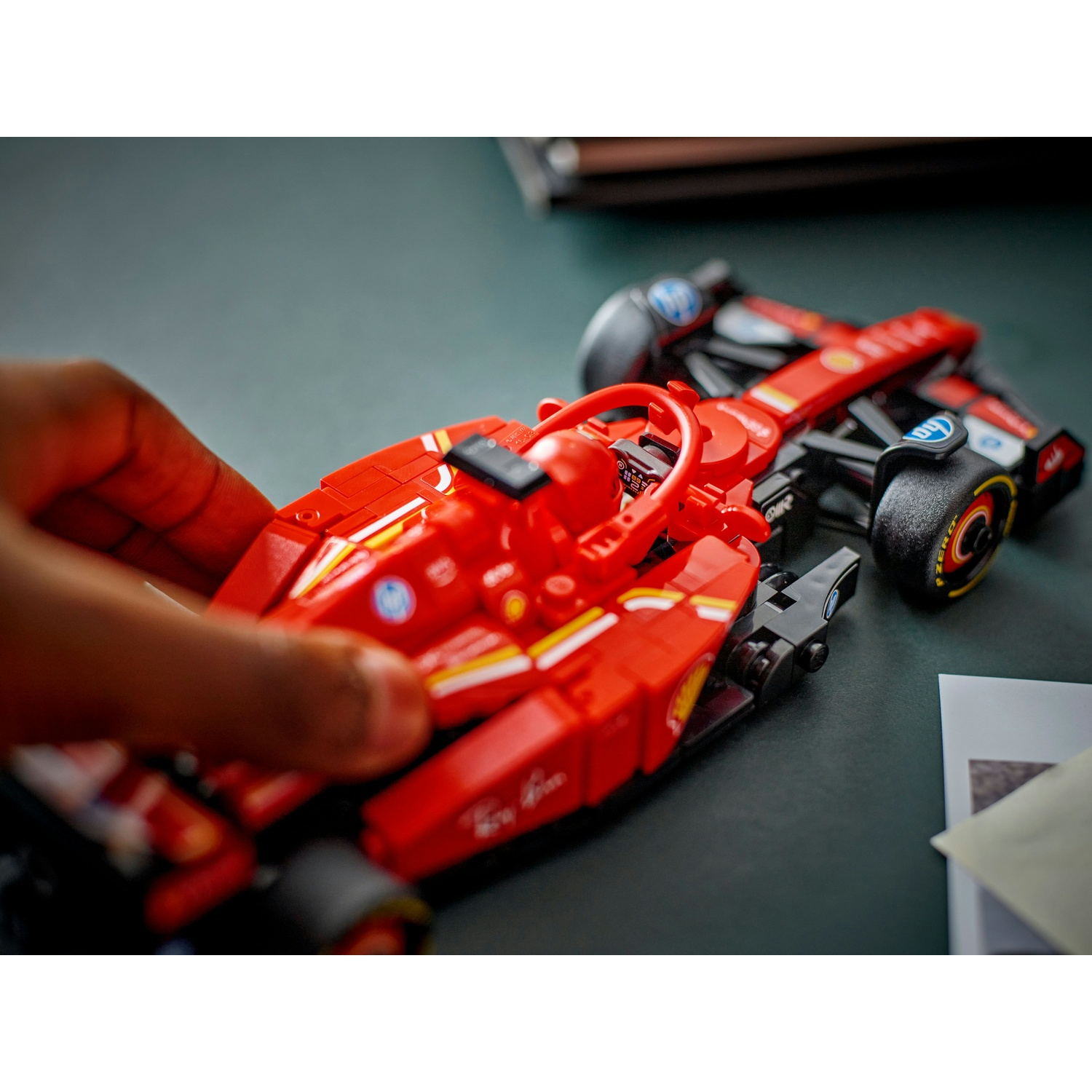 Una mano tiene in mano una Ferrari Lego rossa su una superficie verde scuro. Un'altra macchina sullo sfondo.