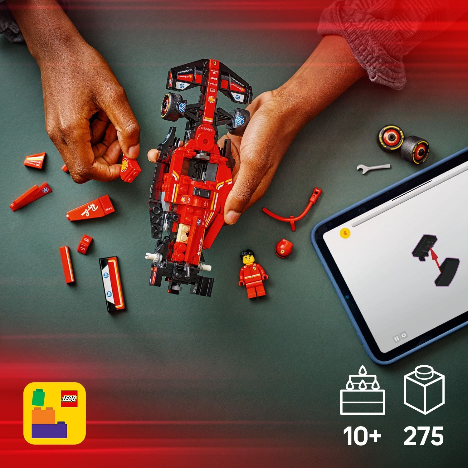 Mani che assemblano un'auto da corsa Lego rossa. Parti e un tablet con istruzioni su una superficie verde scuro. C'è un logo Lego.