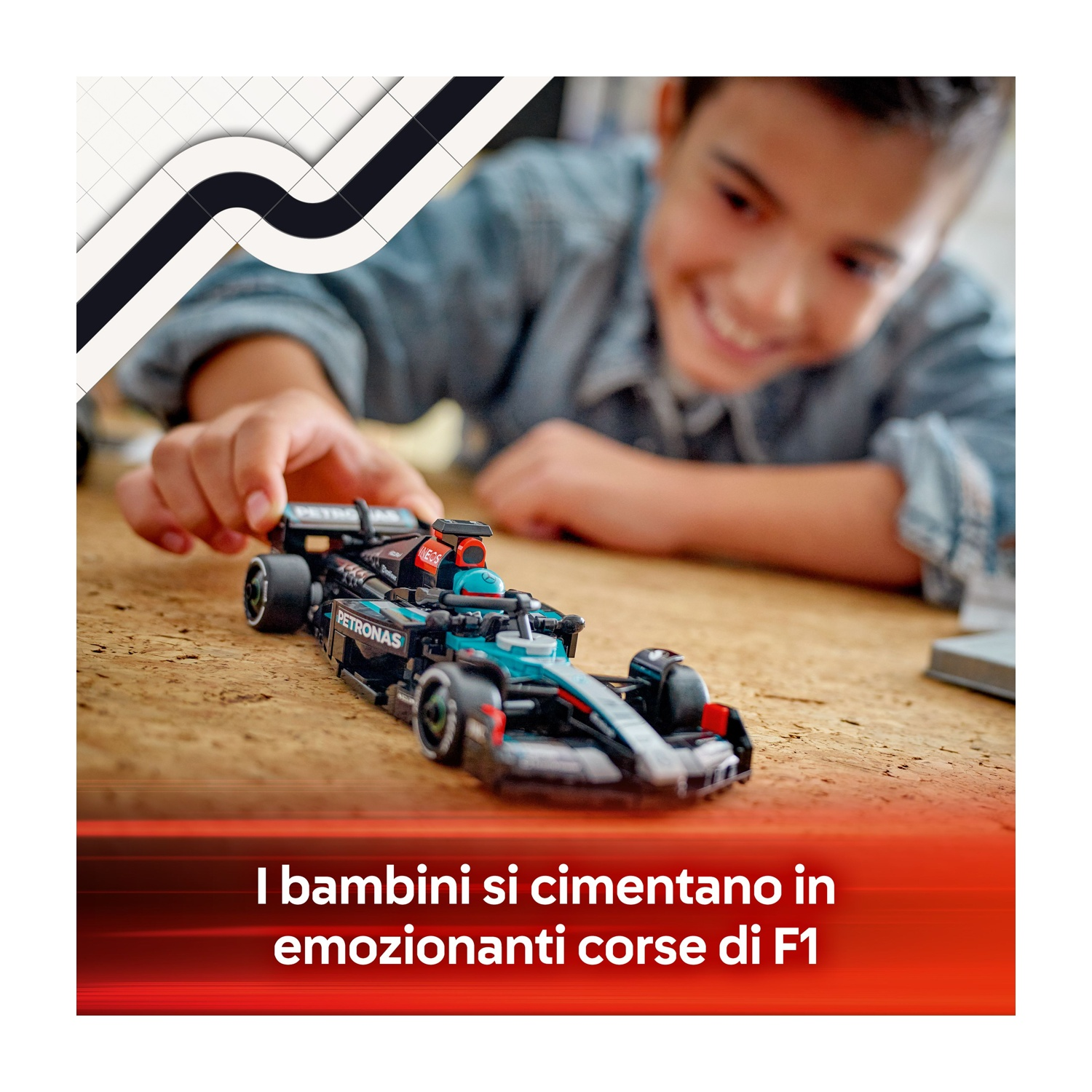 Un ragazzo sorride, gioca con un'auto F1 giocattolo. L'auto è nera e verde acqua, su una superficie di legno. Testo in basso: 'I bambini...'
