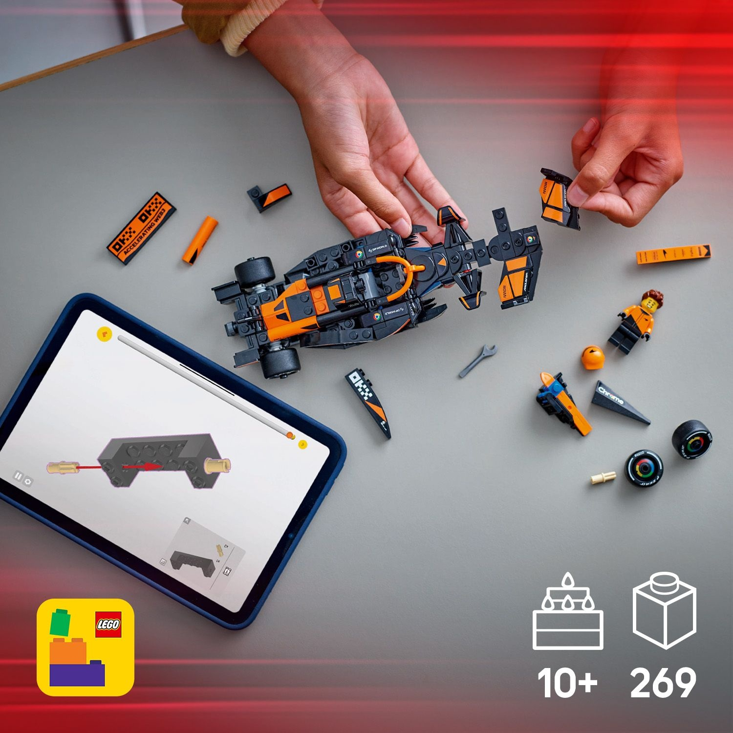 Mani che assemblano un'auto da corsa Lego nera e arancione. Parti sparse attorno a un tablet con istruzioni.