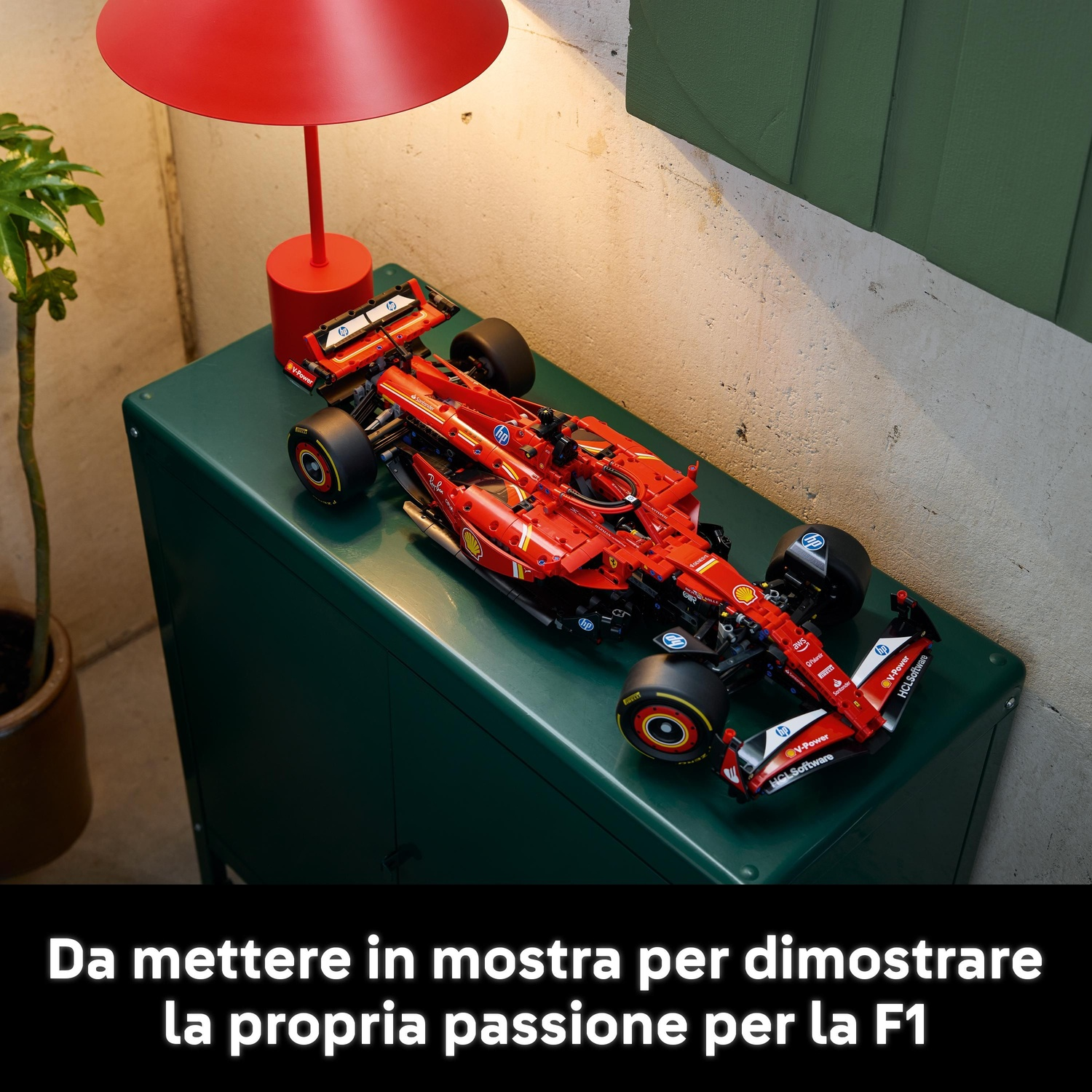 Un'auto di F1 Lego rossa su una superficie verde. Sopra una lampada rossa. A sinistra, una piccola pianta.