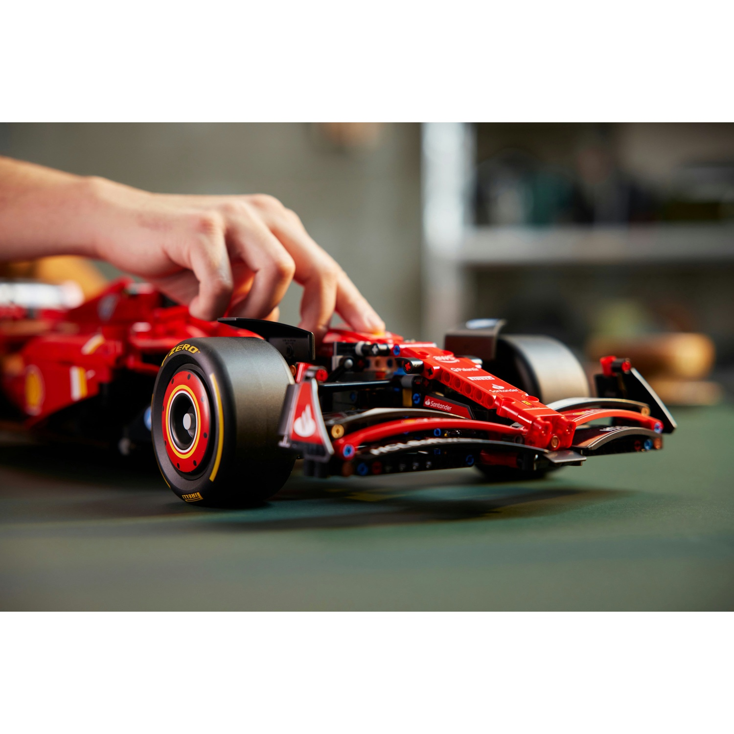 Una mano tocca una Ferrari da corsa Lego rossa su una superficie verde. L'auto ha pneumatici neri e loghi degli sponsor.
