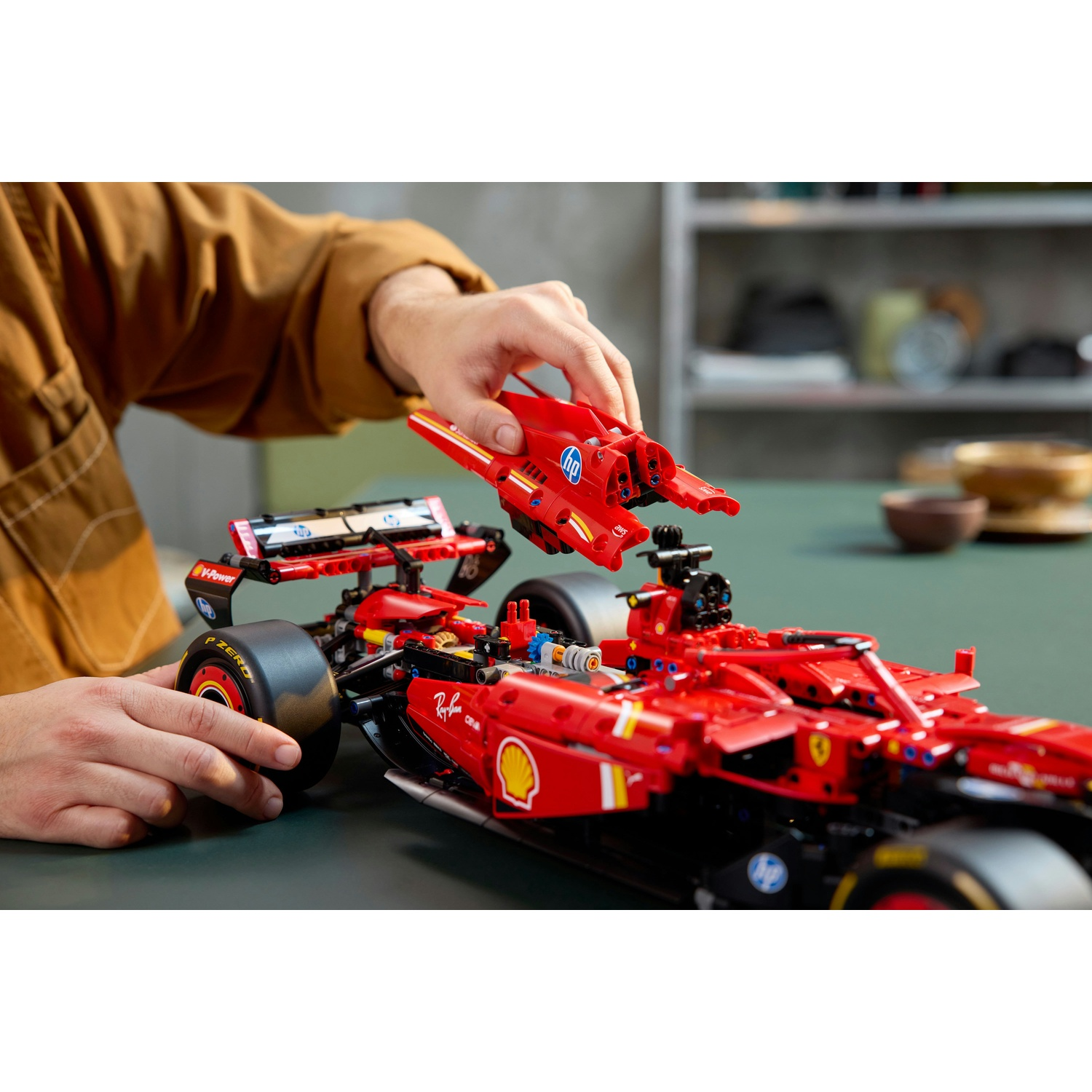 Una persona assembla un modello di auto da corsa Ferrari rossa. L'auto è su una superficie verde, con mensole e ciotole sullo sfondo.